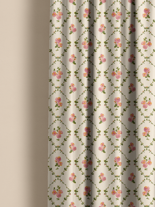 A close-up of a curtain panel with a repeating floral pattern on a warm off-white background, featuring pink roses and green vines. The curtain is shown hanging with soft folds against a neutral beige wall.