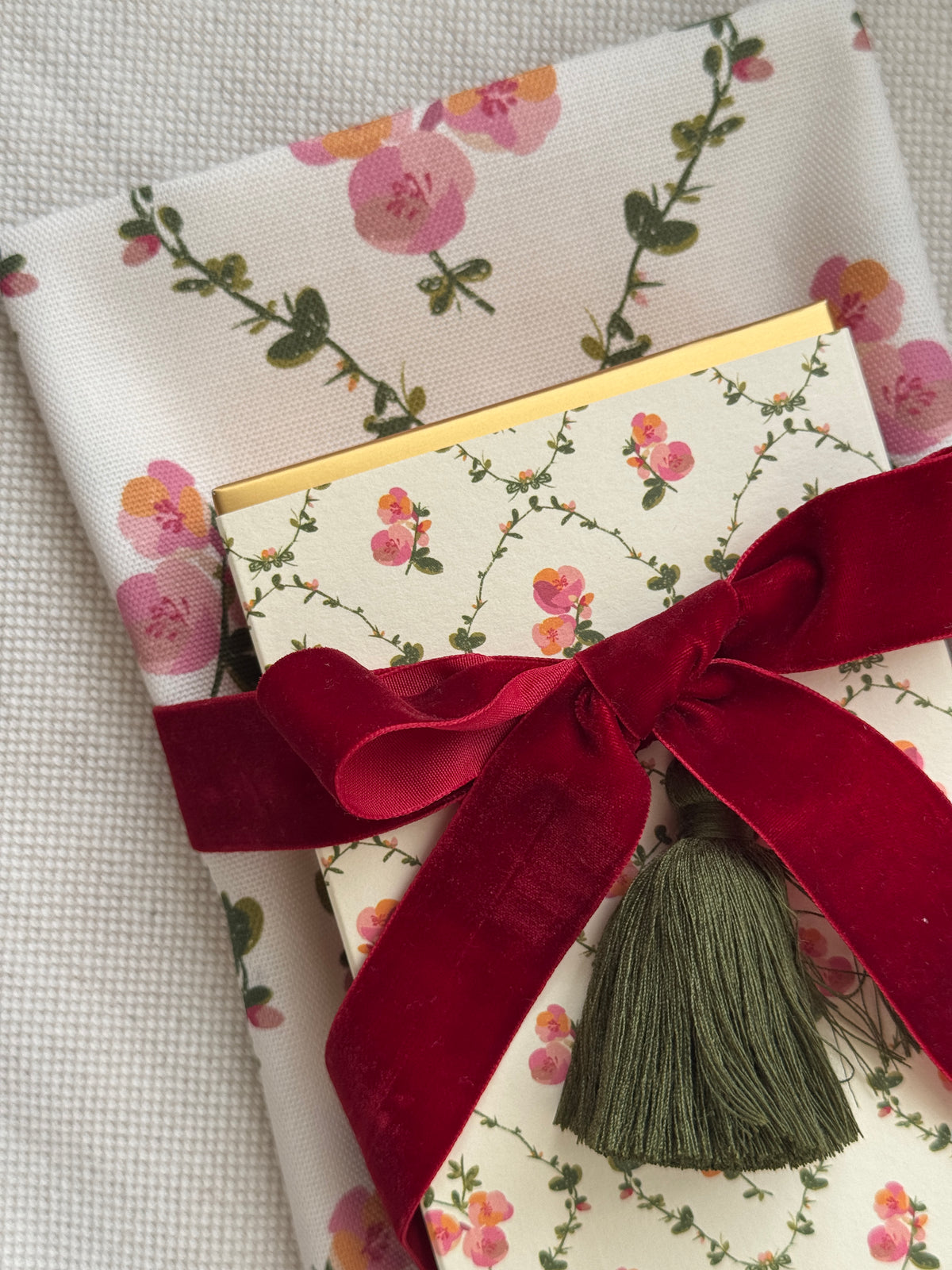 Close up of floral tea towel and decorative matchbox gift set with red velvet ribbon.