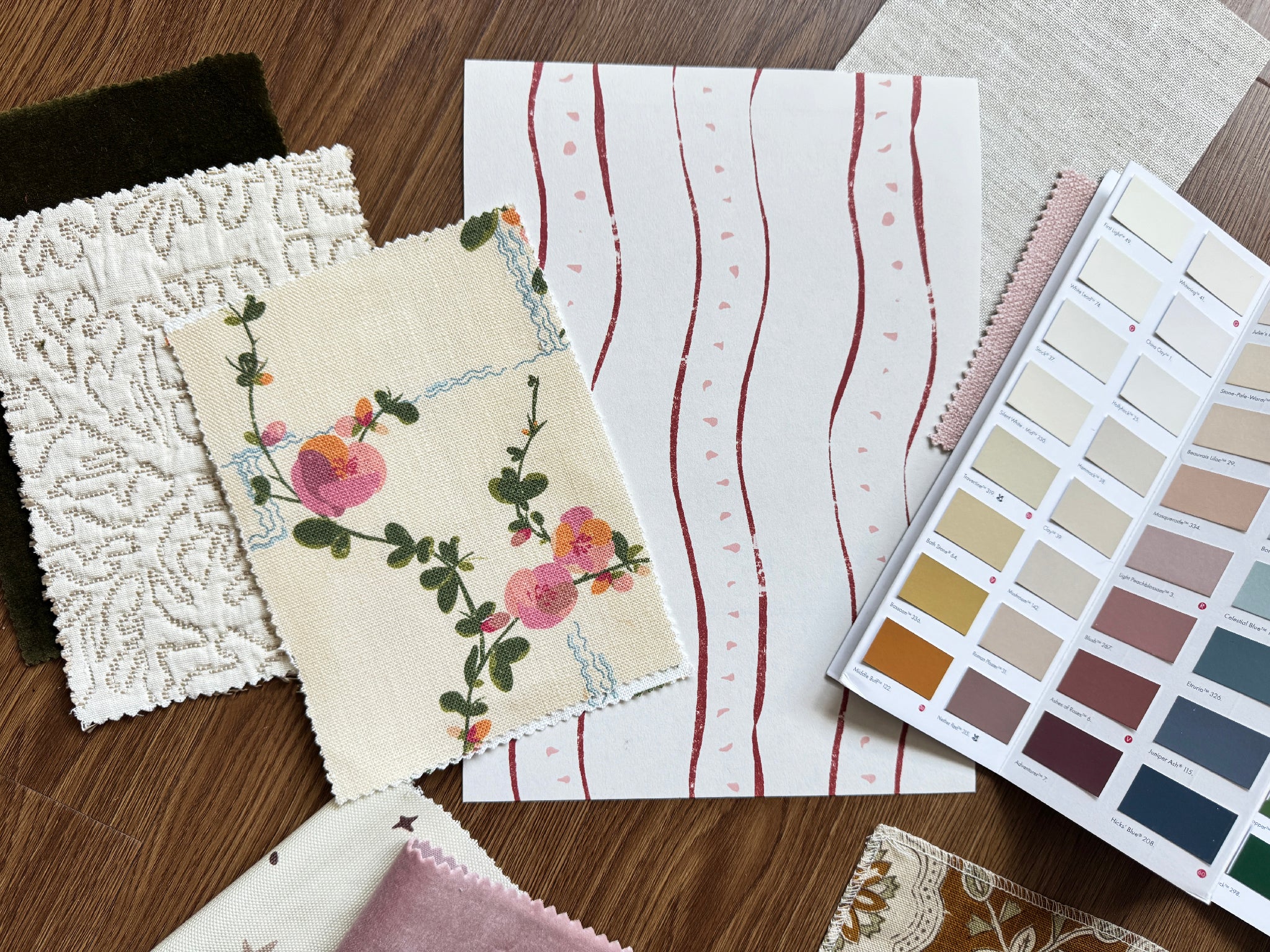 Layered Fabric and wallpaper swatches memos and color chart on a wooden surface.